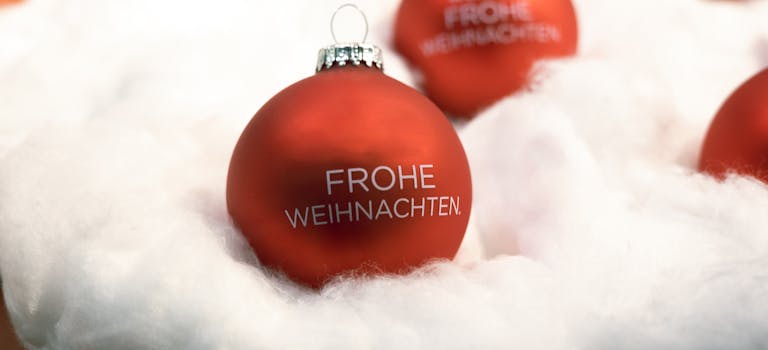 Close-up of a red Christmas ornament with 'Frohe Weihnachten' on fluffy snow-like material.