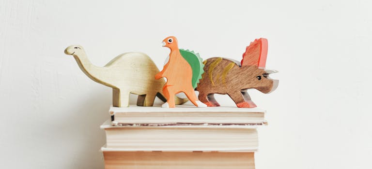 Colorful wooden dinosaurs on top of a stack of hardcover books on a light background.