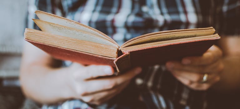 Close-up of hands holding and reading an antique book indoors, symbolizing knowledge and learning.