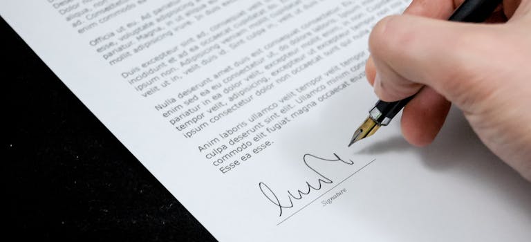 Close-up of a hand signing a formal document with a fountain pen, indicating agreement.