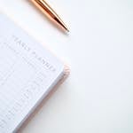A stylish yearly planner open to a 2020 calendar page, accompanied by a golden pen on a clean white surface.