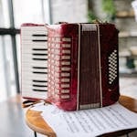 A vibrant red accordion and sheet music on a stool in an indoor setting.