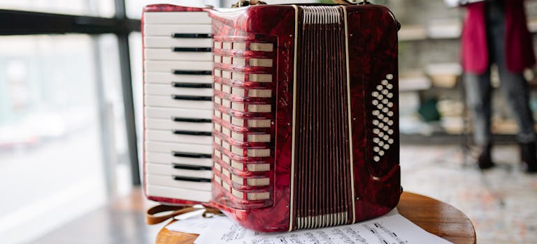 A vibrant red accordion and sheet music on a stool in an indoor setting.