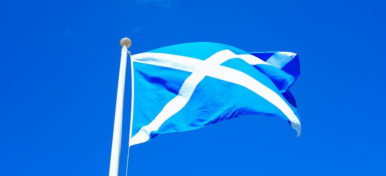 Scottish flag on a pole set against a vivid blue sky with scattered clouds.
