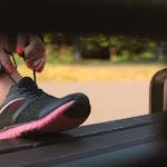 Close-up of a woman tying her athletic shoes on a bench in a park, preparing for a run.