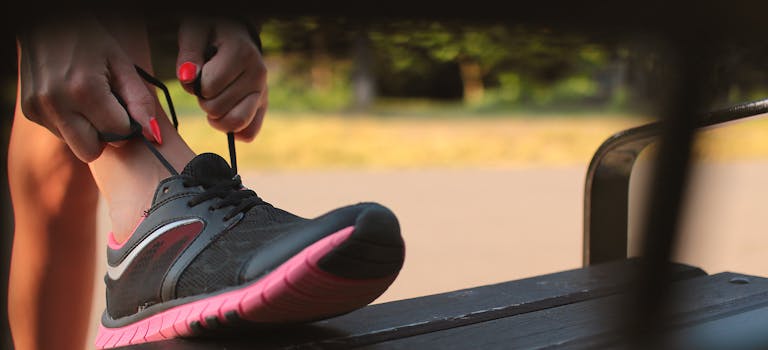 Close-up of a woman tying her athletic shoes on a bench in a park, preparing for a run.