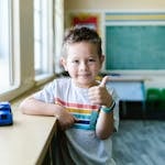 Smiling child in a classroom giving a thumbs up, symbolizing confidence and joy.