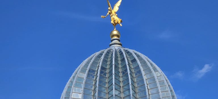 A striking view of the Dresden Academy of Fine Arts dome with a golden sculpture against a blue sky.