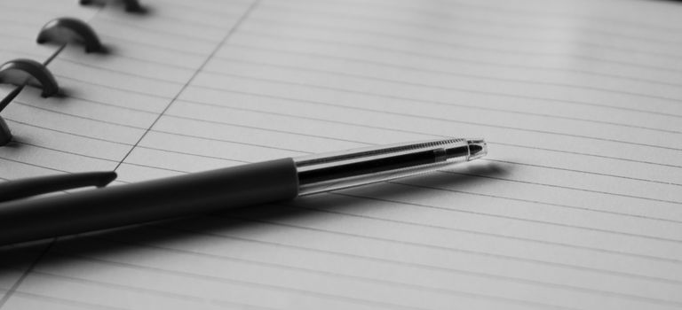 Black and white image of a pen resting on an open lined notebook, ideal for writing or note-taking themes.